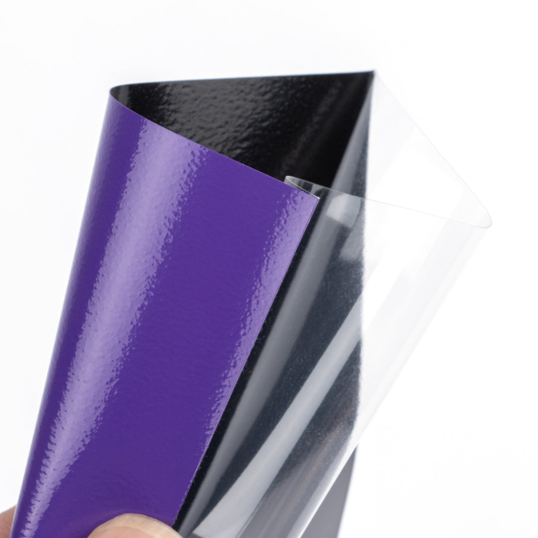 Purple, black, and clear deck protector sleeve held by a hand on a white background