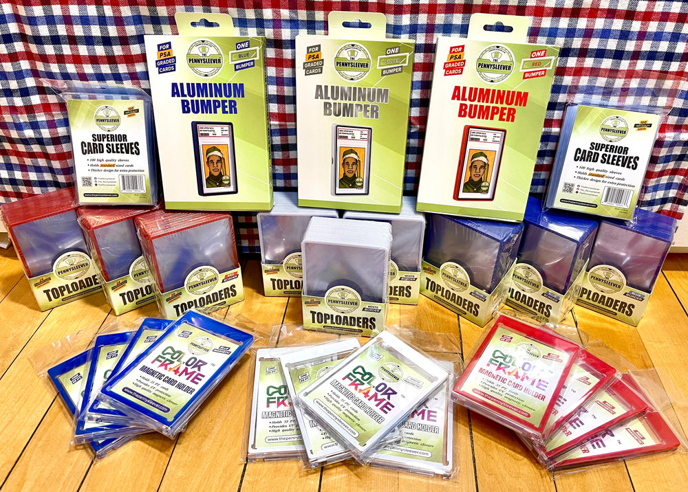 A collection of card protection products including aluminum bumpers, top loaders, and card sleeves in multiple colors, arranged on a wooden floor in front of a red, white, and blue plaid backdrop.