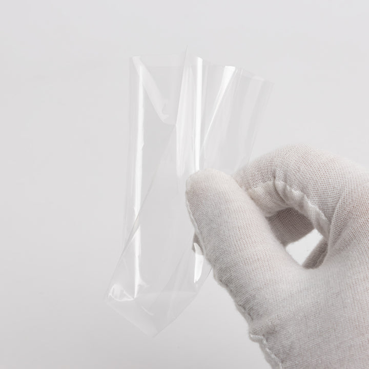 A single card sleeve being held up by a gloved hand against a white background.