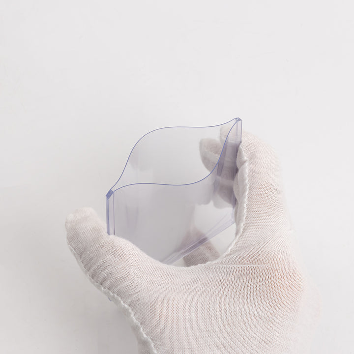 A white gloved hand squeezing a 35 point toploader against a white backdrop.
